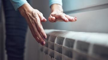 Woman heating her hands over a radiator.