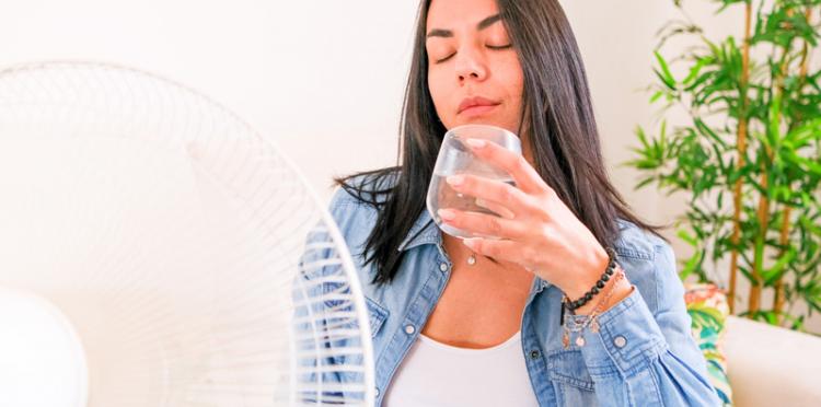 A woman using a fan and staying hydrated during a heat wave.