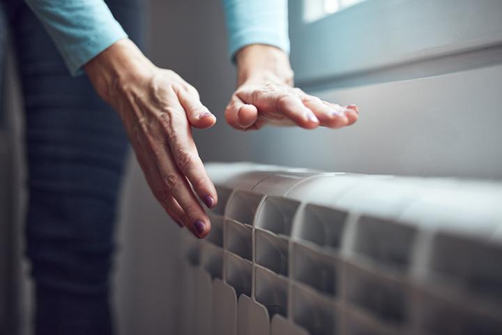 Woman heating her hands over a radiator.