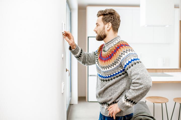 Man in sweater adjusting thermostat