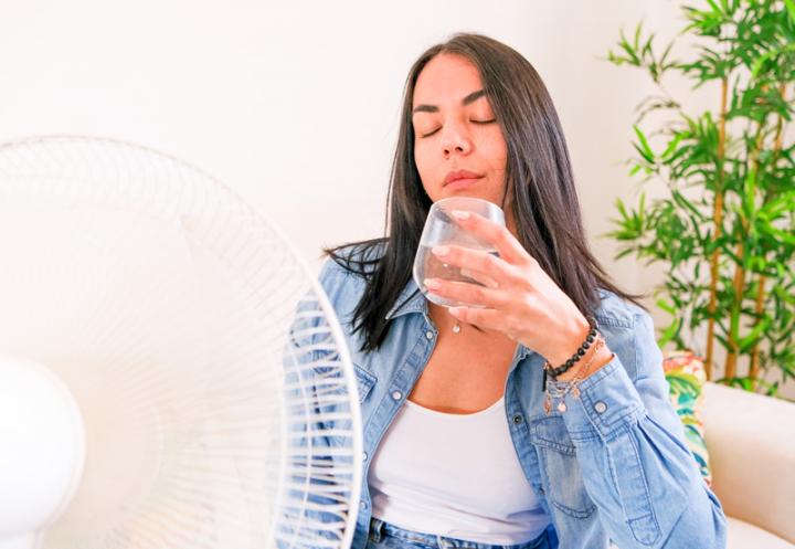 A woman using a fan and staying hydrated during a heat wave.